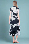 Woman wearing a black dress with white floral patterns against a white wall.