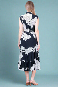Woman wearing a black dress with white floral patterns against a white wall.