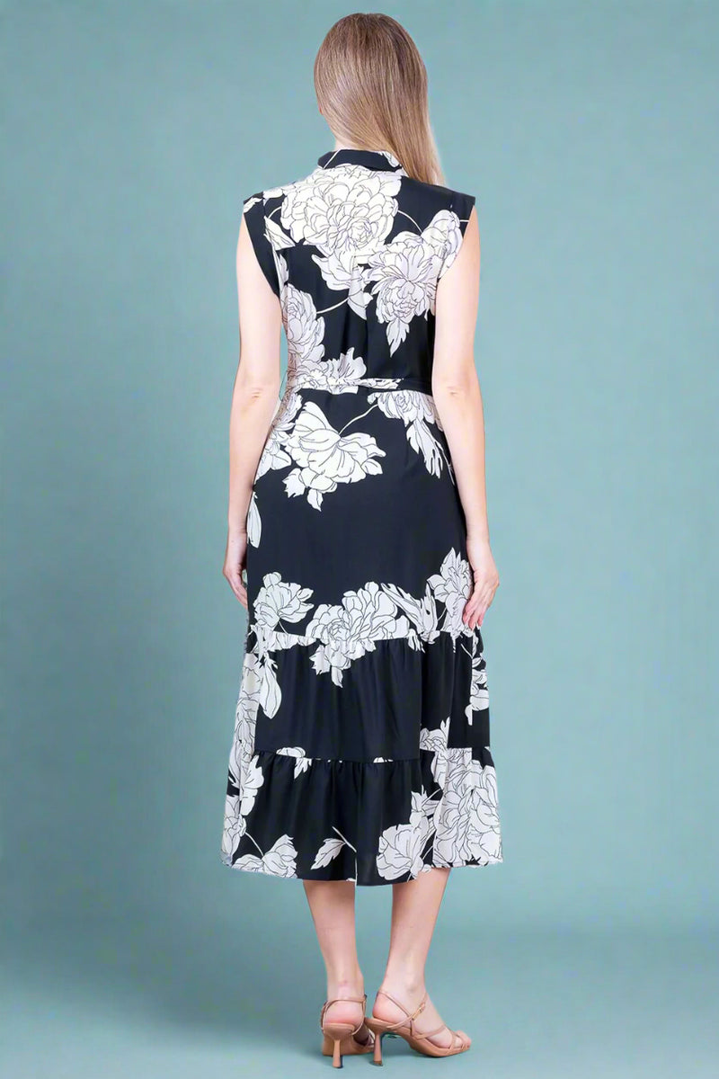 Woman wearing a black dress with white floral patterns against a white wall.