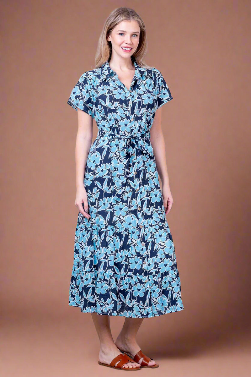 Woman wearing a blue floral dress against a white wall.
