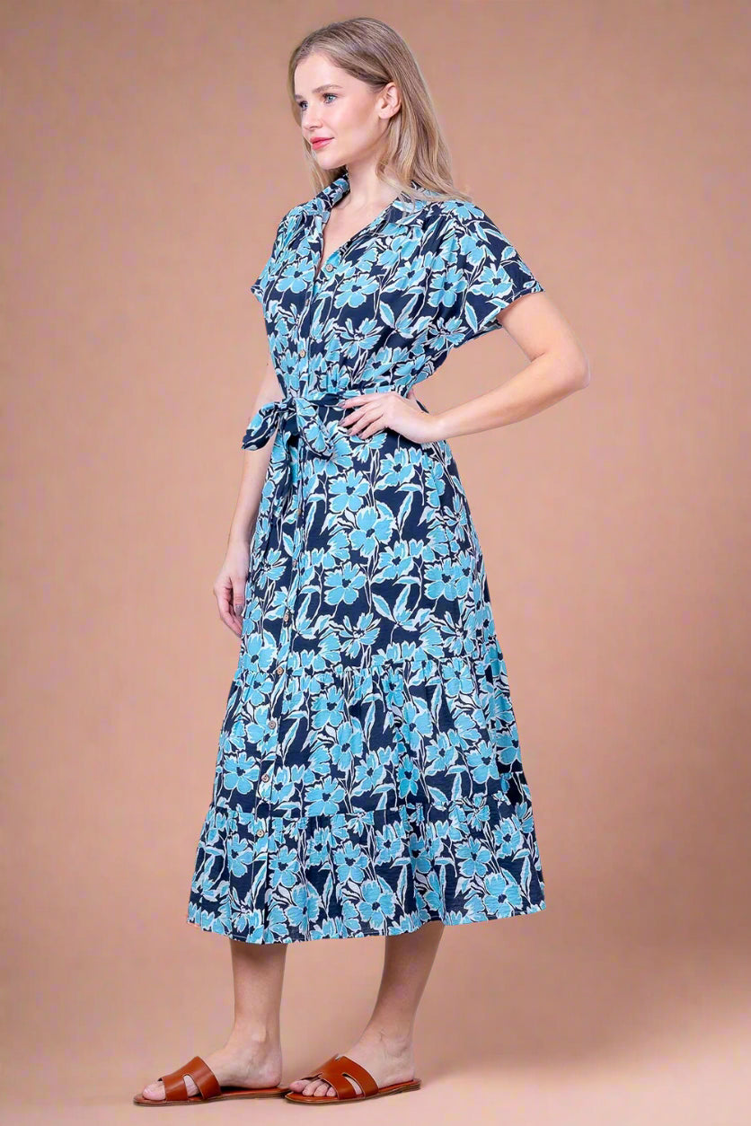 Woman wearing a blue floral dress against a white brick wall.