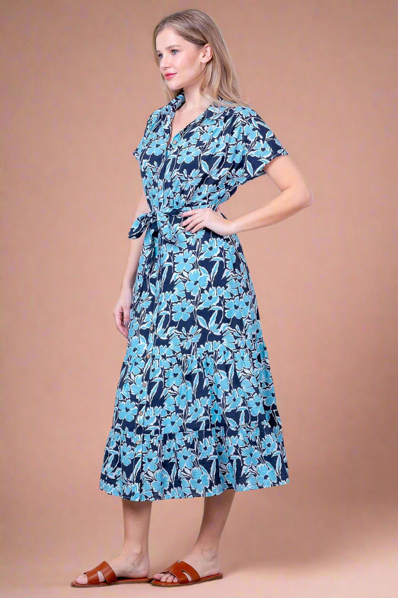 Woman wearing a blue floral dress against a white brick wall.