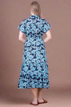 Woman wearing a blue floral dress against a white brick wall.