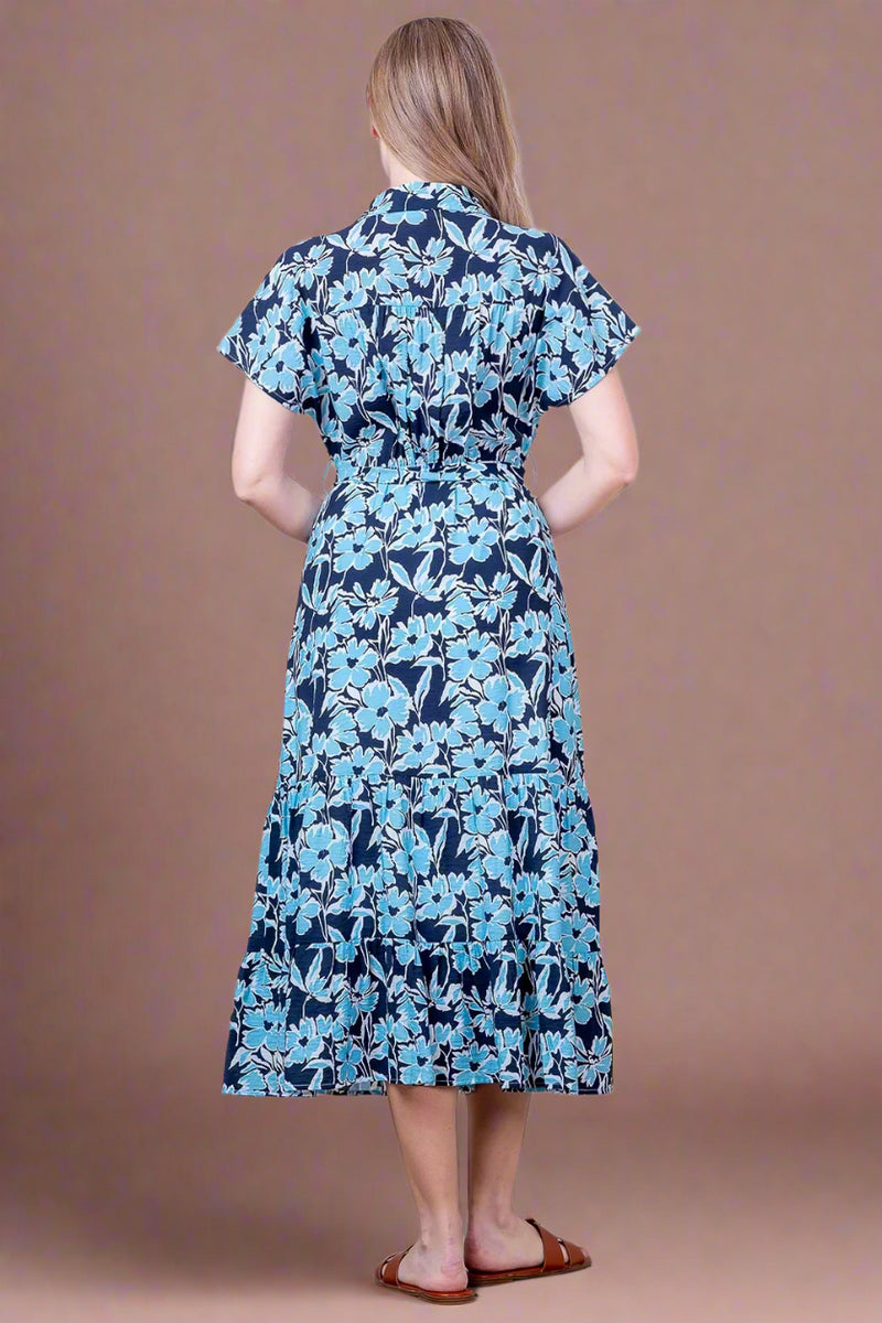 Woman wearing a blue floral dress against a white brick wall.