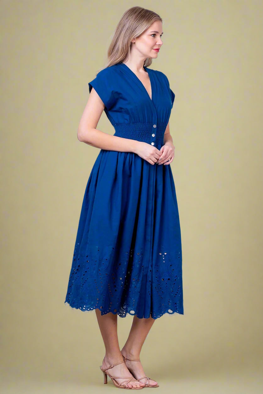 Woman wearing a blue dress against a white brick wall.