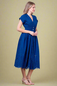 Woman wearing a blue dress against a white brick wall.