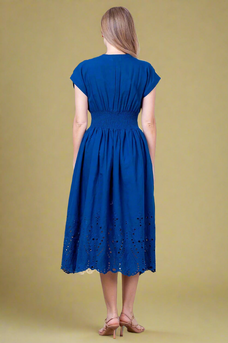 Woman wearing a blue dress standing against a white wall.