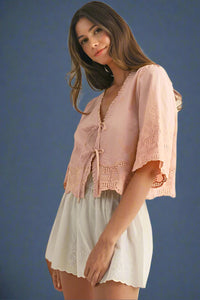 Woman wearing a pink lace top and white shorts on a beige background