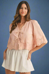 Woman wearing a pink lace top and white shorts on a beige background