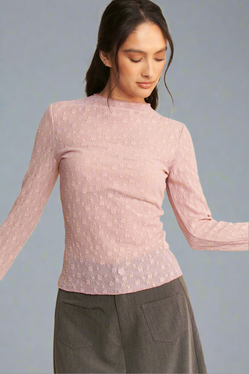 Model is wearing a textured semi sheer mesh top with a lettuce hem and slight mock neck.