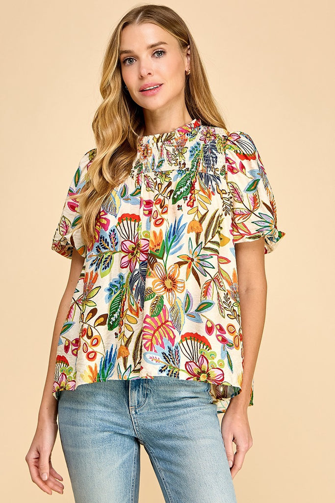 Model is wearing a smocked, short puff sleeve top in a colorful floral pattern.