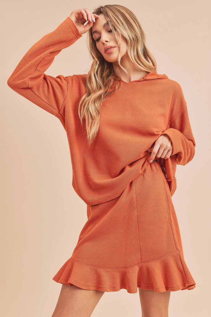 This hooded top is an ochre orange color. It has long sleeves and is made form soft fabric.