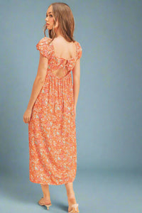 Woman wearing a floral dress with cut-out back on a beige background