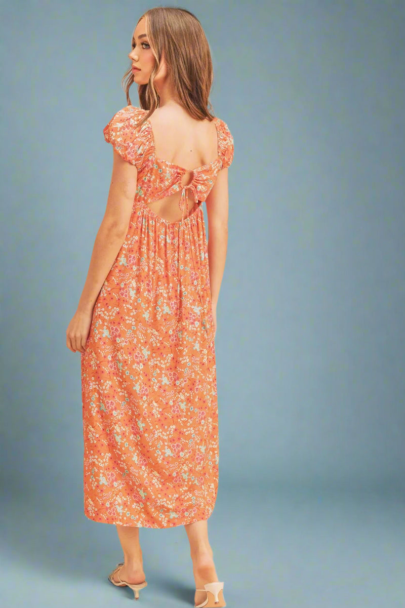 Woman wearing a floral dress with cut-out back on a beige background