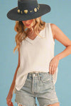 Woman wearing a white sleeveless top and denim shorts with a dark blue hat on a beige background