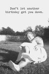 A greeting card with old black and white photo of an older woman laying in the grass with the text ‘Don’t let another birthday get you down.’