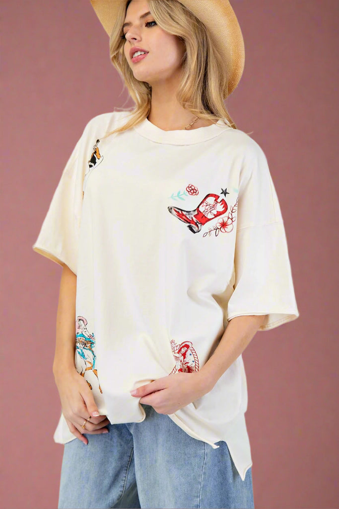 Model is wearing an oversized ivory tee with a western print design and rolled hems.