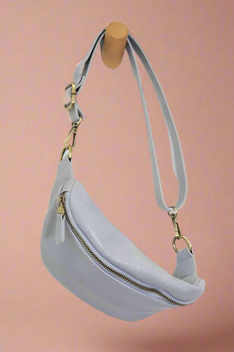 A sling bag n light blue. It has a zipper closure and brass plated accents.