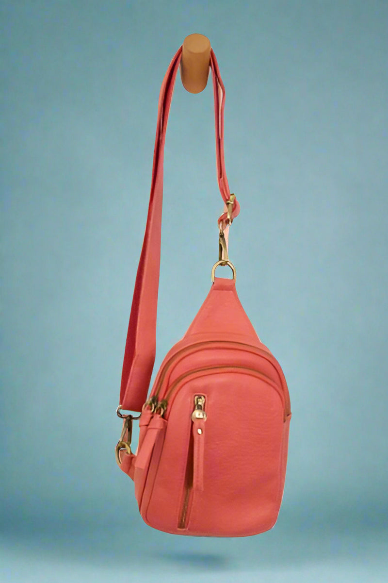 Adjustable, coral, sling bag with brass hardware and several, zippered compartments.