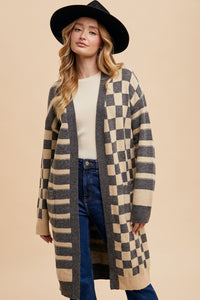 A women’s knee length, medium weight open knit cardigan featuring a mixed print of grey and tan checks and stripes with two front pockets.