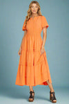 Woman wearing an orange tiered maxi dress on a plain background
