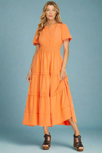 Woman wearing an orange tiered maxi dress on a plain background