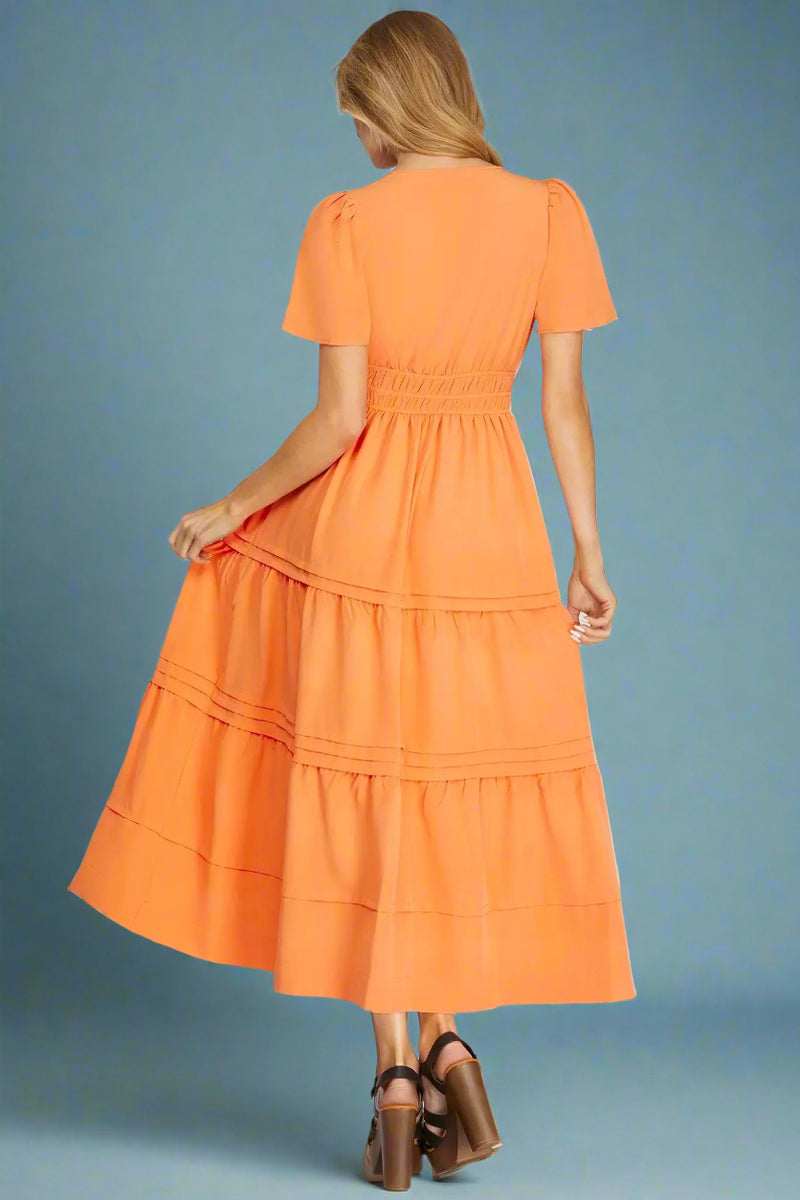 Orange tiered dress worn by a model on a plain background