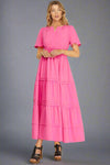 Woman wearing a pink tiered maxi dress on a plain background