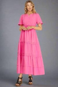 Woman wearing a pink tiered maxi dress on a plain background
