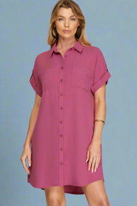 Woman wearing a magenta button-up dress against a plain background