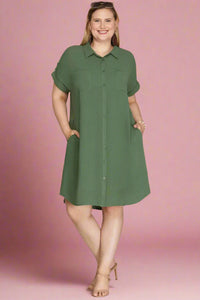 Woman wearing a green button up shirt dress against a plain background