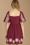 Maroon dress with white floral patterns on sleeves and hem against a plain background
