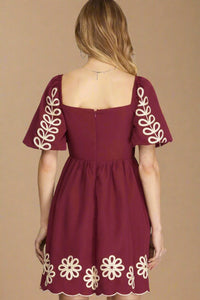 Maroon dress with white floral patterns on sleeves and hem against a plain background