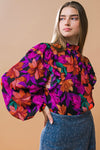This woven top has a ruffled high neck, shoulder ruffles, and a smocked cuff. It s a bright colored floral pattern.