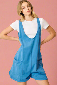 Model is wearing a bright blue overall style romper with deep pockets and adjustable straps. 
