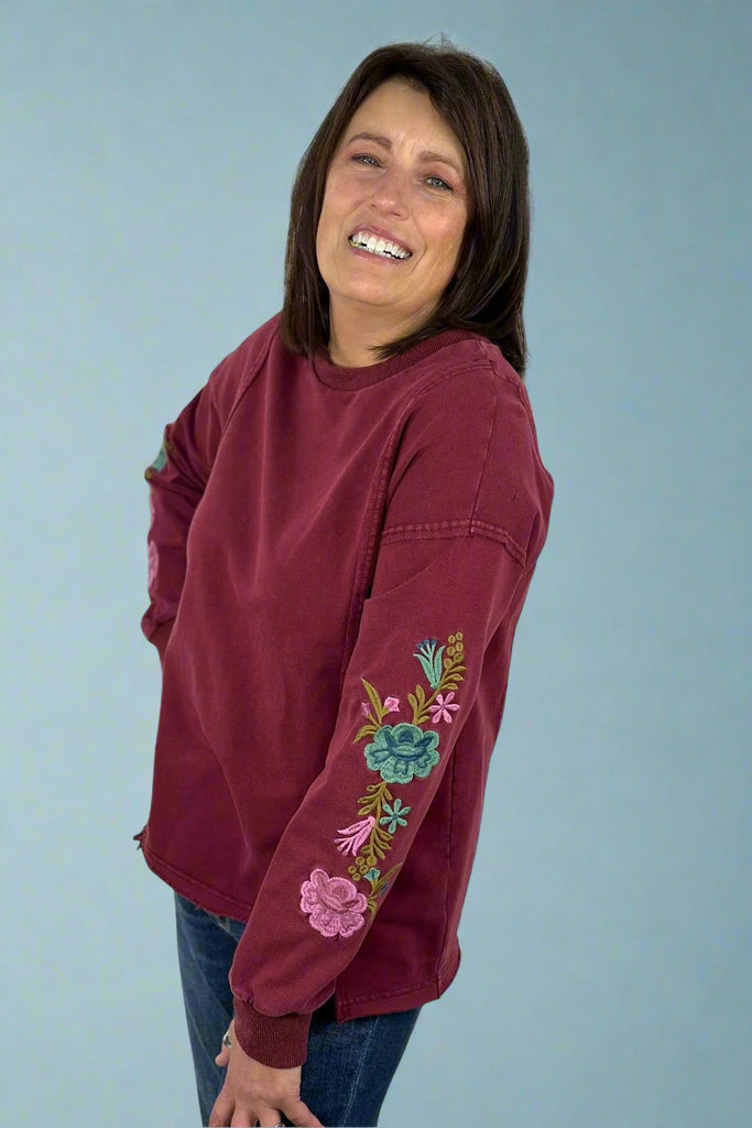 Crewneck lightweight sweatshirt top in a vintage burgundy color. Colorful floral embroidery on sleeve. Raw hem detail. 