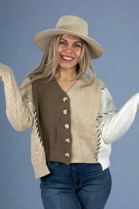 Model is wearing a long sleeve mixed knit cardigan. The cardigan has medium sized buttons, contrasting exposed stitch details and an asymmetrical hem. With a slight crop it hits at hip length. 