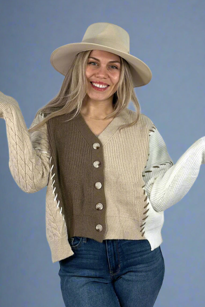 Model is wearing a long sleeve mixed knit cardigan. The cardigan has medium sized buttons, contrasting exposed stitch details and an asymmetrical hem. With a slight crop it hits at hip length. 