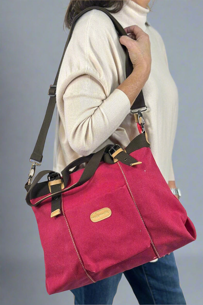 Model holds the Vivian Convertible Canvas bag in Raspberry Red. This weekender bag features a deep red base with dark brown straps and a front pocket.