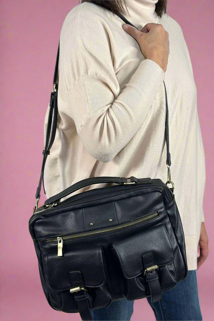 Model wears black messenger bag with long front zipper and two, front, buckled pockets.