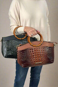 Model shows cases The Phoebe Faux Crocodile Tote in black and cognac, both featuring a circular wooden handle and complemented by faux crocodile skin/ faux leather body.