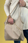 Model holds mid-size, beige, vegan leather shoulder bag with matching cosmetic bag.