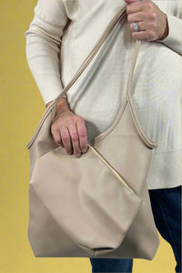 Model holds mid-size, beige, vegan leather shoulder bag with matching cosmetic bag.