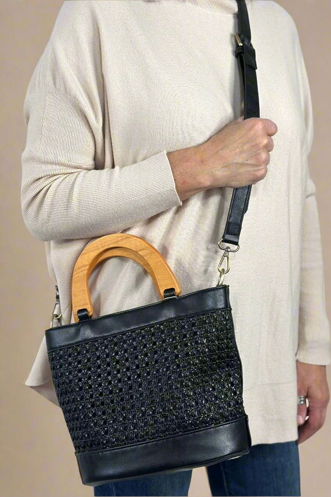 A black satchel with a braided patter. It has a crossbody strap and wood handle.