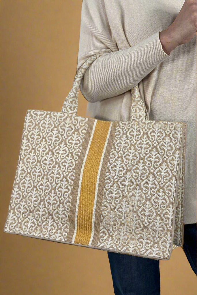 A tote bag in sand, white, and mustard. Has a large, open interior with an additional two interior pockets.