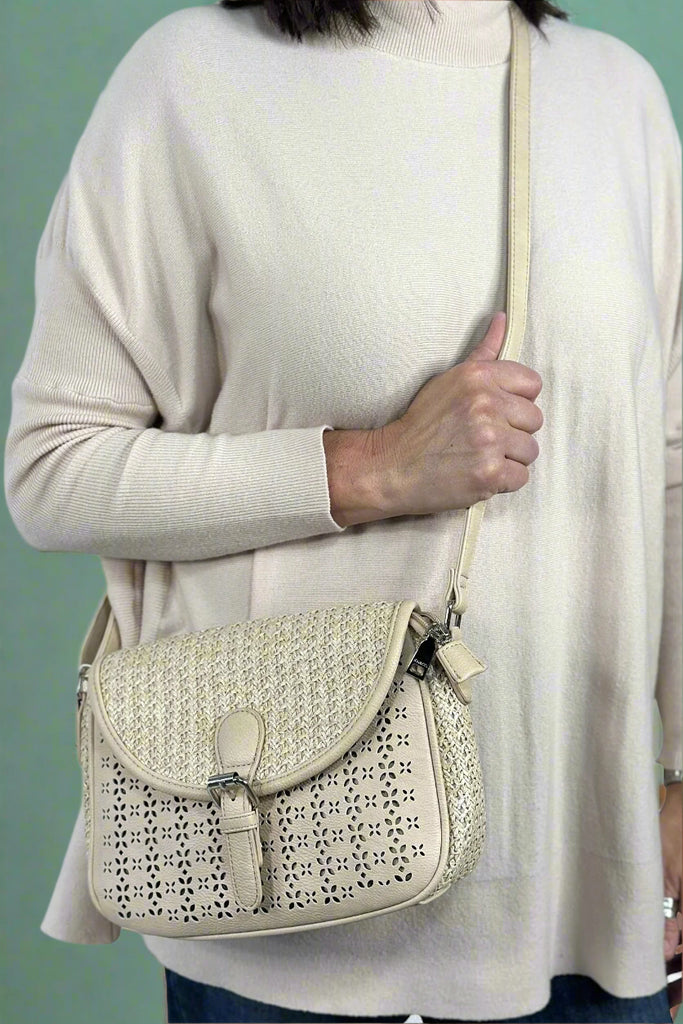 Cream colored crossbody with a perforated leather front panel and contrasting straw side panels and front flat. 