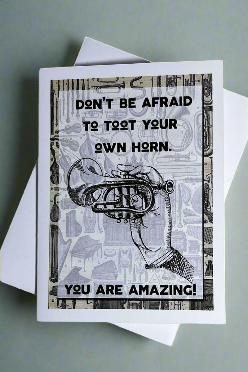 A greeting card that says “Don’t Be Afraid To Toot Your Own Horn” with an image of a hand holding a horn.