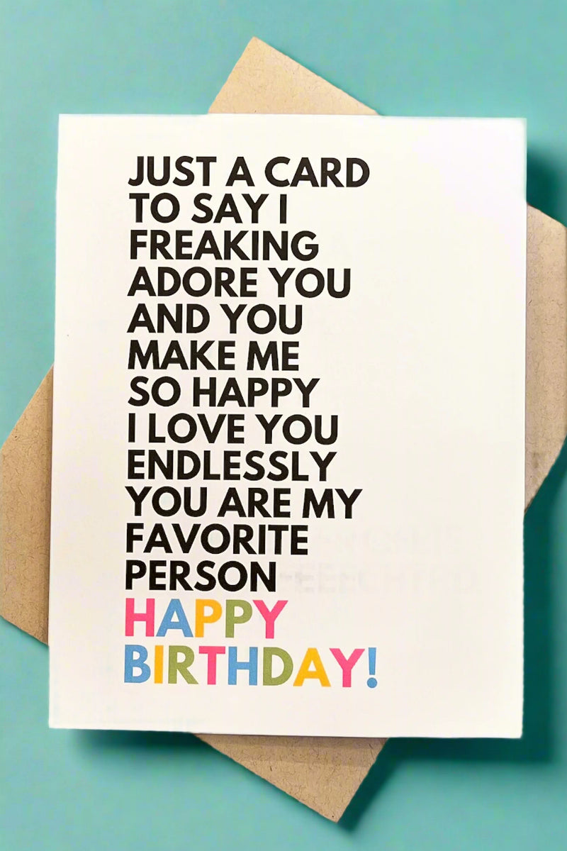 A solid white greeting card with black text that reads ‘Just a card to say I freaking adore you and you make me so happy. I love you endlessly. You are my favorite person. Happy Birthday!’