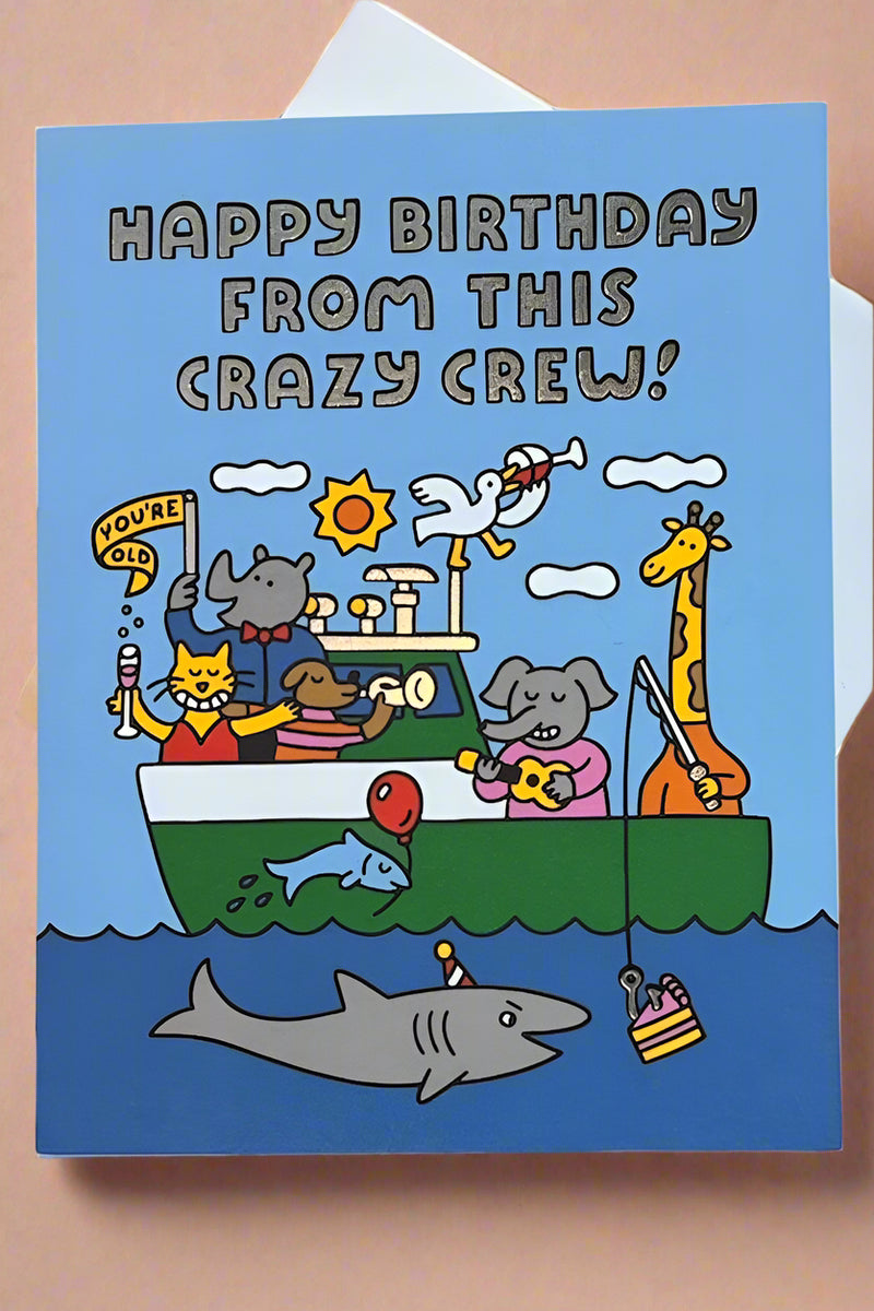 A greeting card with the image of a boat full of animals doing random things like playing music and drinking with text that reads ‘Happy Birthday From This Crazy Crew!’