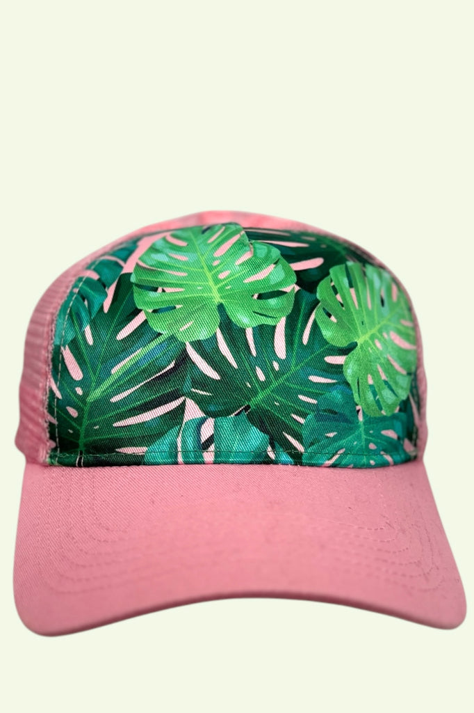 Pink mesh back trucker hat with green monstera leafs printed across the front panel. 